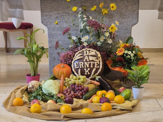 Ein Kirchenaltar ist für das Erntedankfest geschmückt. Auf den Stufen liegen Früchte wie Kürbisse, Trauben und Zitronen sowie Blumen. In der Mitte ein Schild mit 'DA ERNTE K'. Ein weißes Tuch über dem Altar trägt die Aufschrift 'Mein Herr und mein Gott!'.